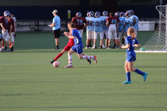 Two soccer teams playing in a game on the Pier 40 Courtyard Fields, with a football team in the background