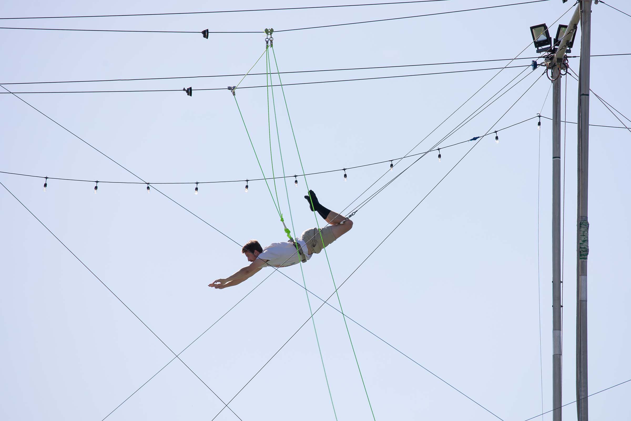 A trapeze artist swings and reaches for the bar in the air