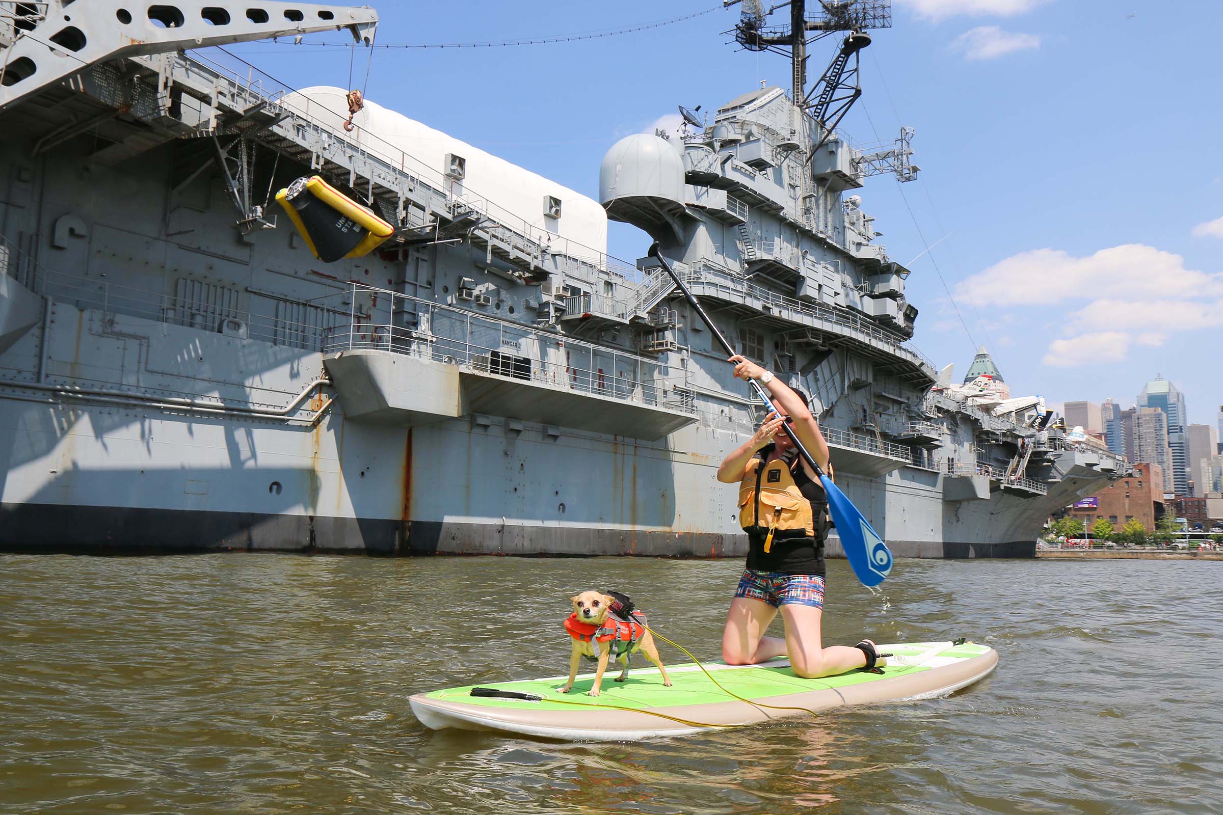 A dog and its owner paddle board next to the massive Intrepid vessel