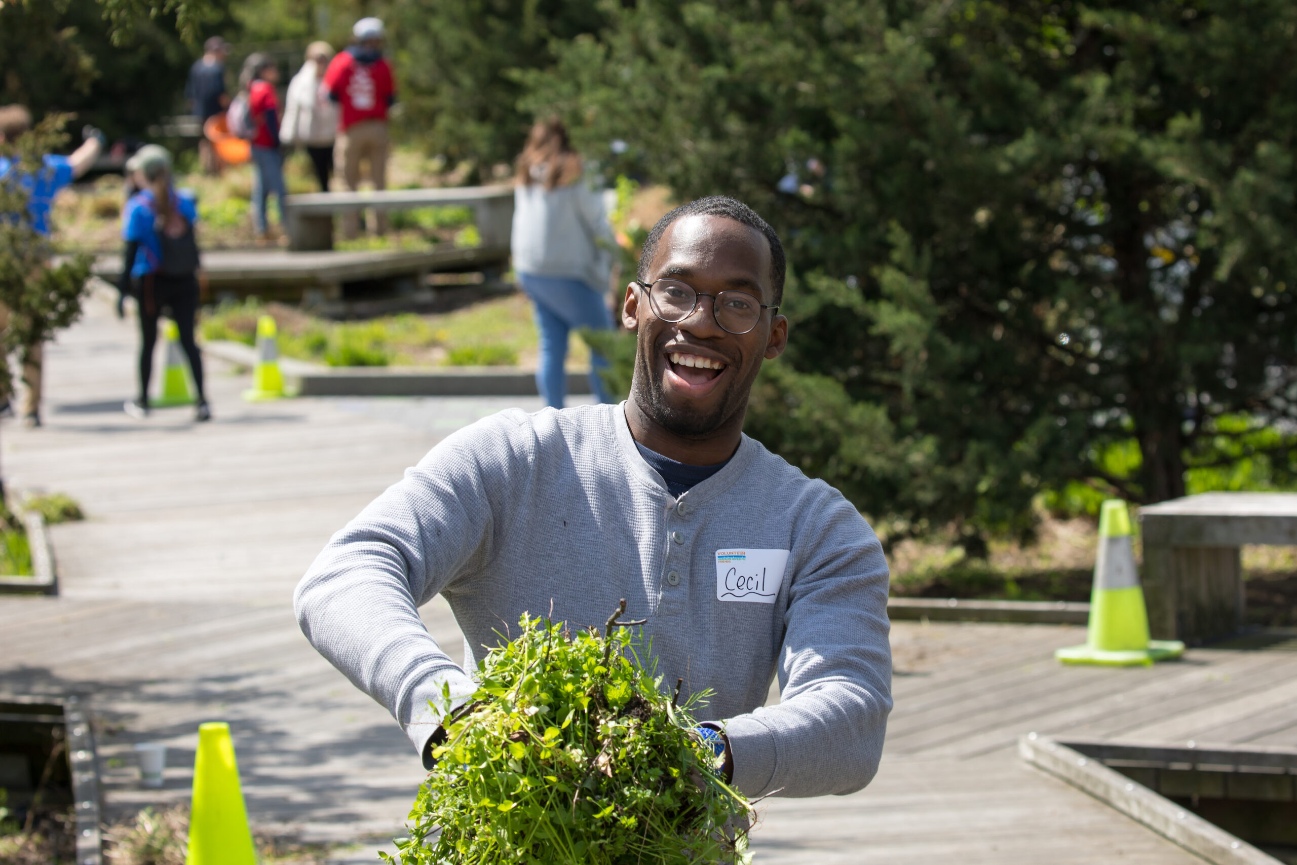 A volunteer smiles and holds a potted plant toward the camera