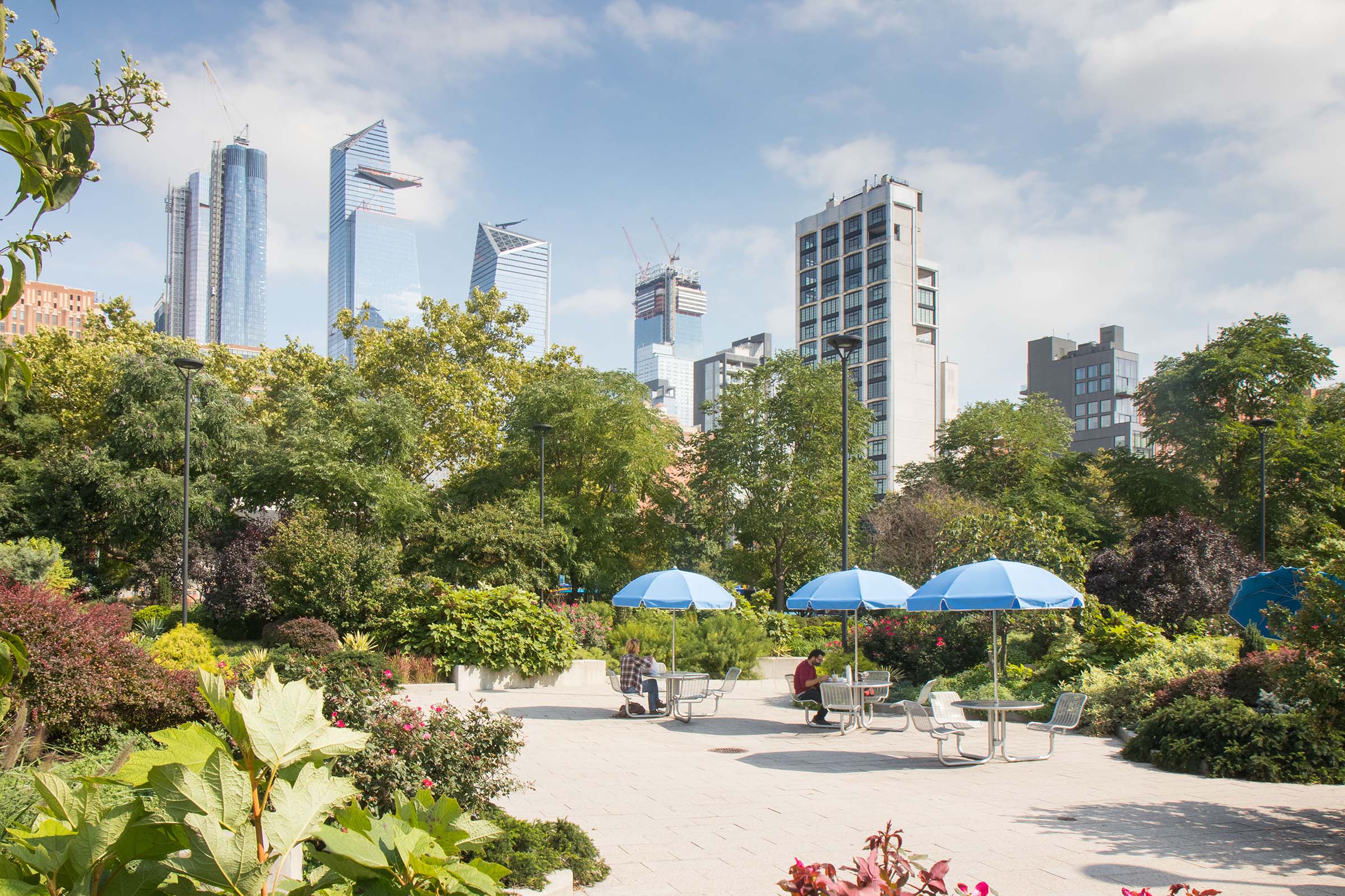Blue umbrellas shade Park visitors at the tables in the Chelsea Entry Garden
