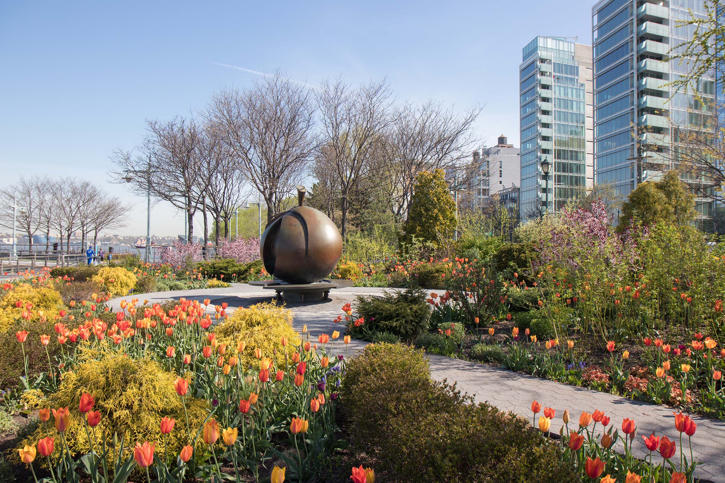 Lush green and yellow bushes and tulips circle the bronze Apple statue