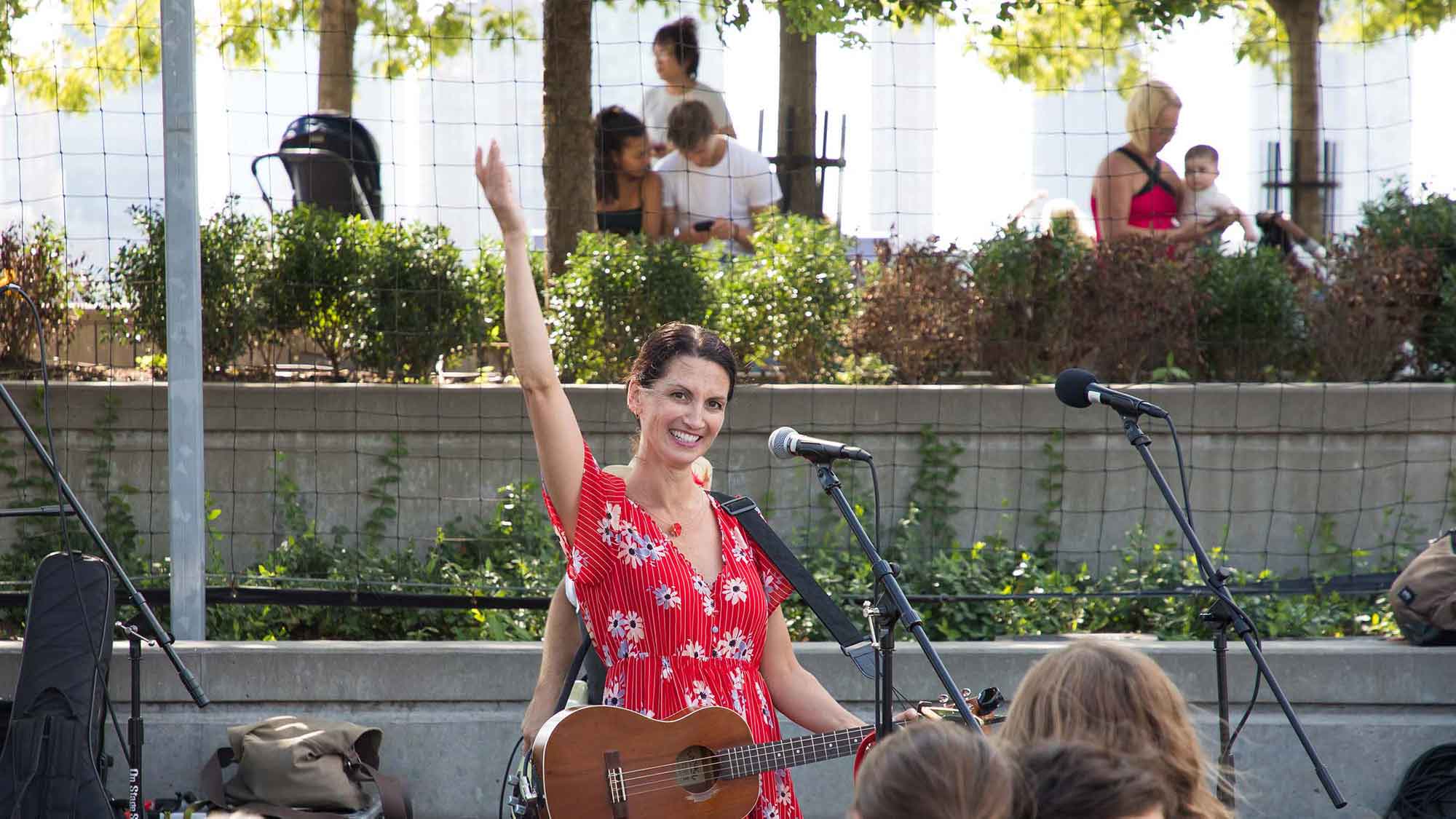 Suzi Shelton in a red dress with flowers raises her hand as she sings