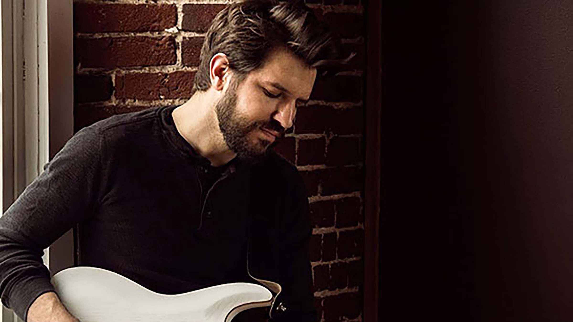 Zach Comtois plays his white electric guitar as looks down in thought