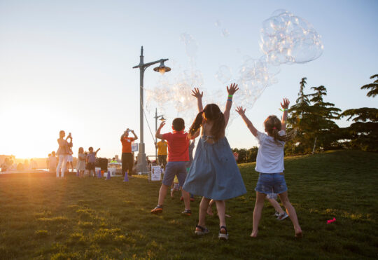 The sun sets at the kids raise their hands and sing at the bbq