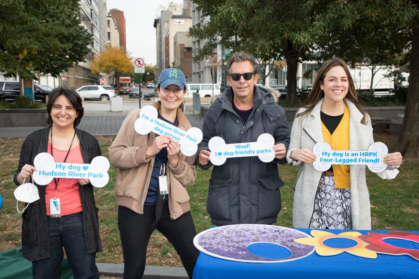 Hudson River Park Friends hold up branded signs to promote HRPK's Four-Legged Friends program at Barktoberfest