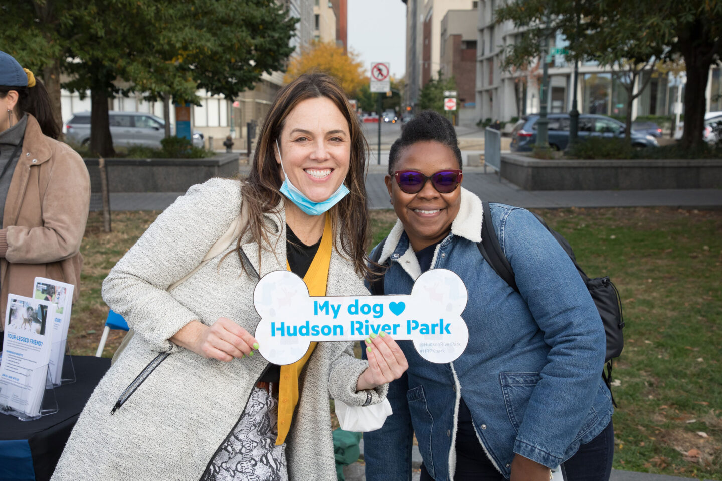 Hudson River Park Friends hold up branded signs to promote HRPK's Four-Legged Friends program at Barktoberfest