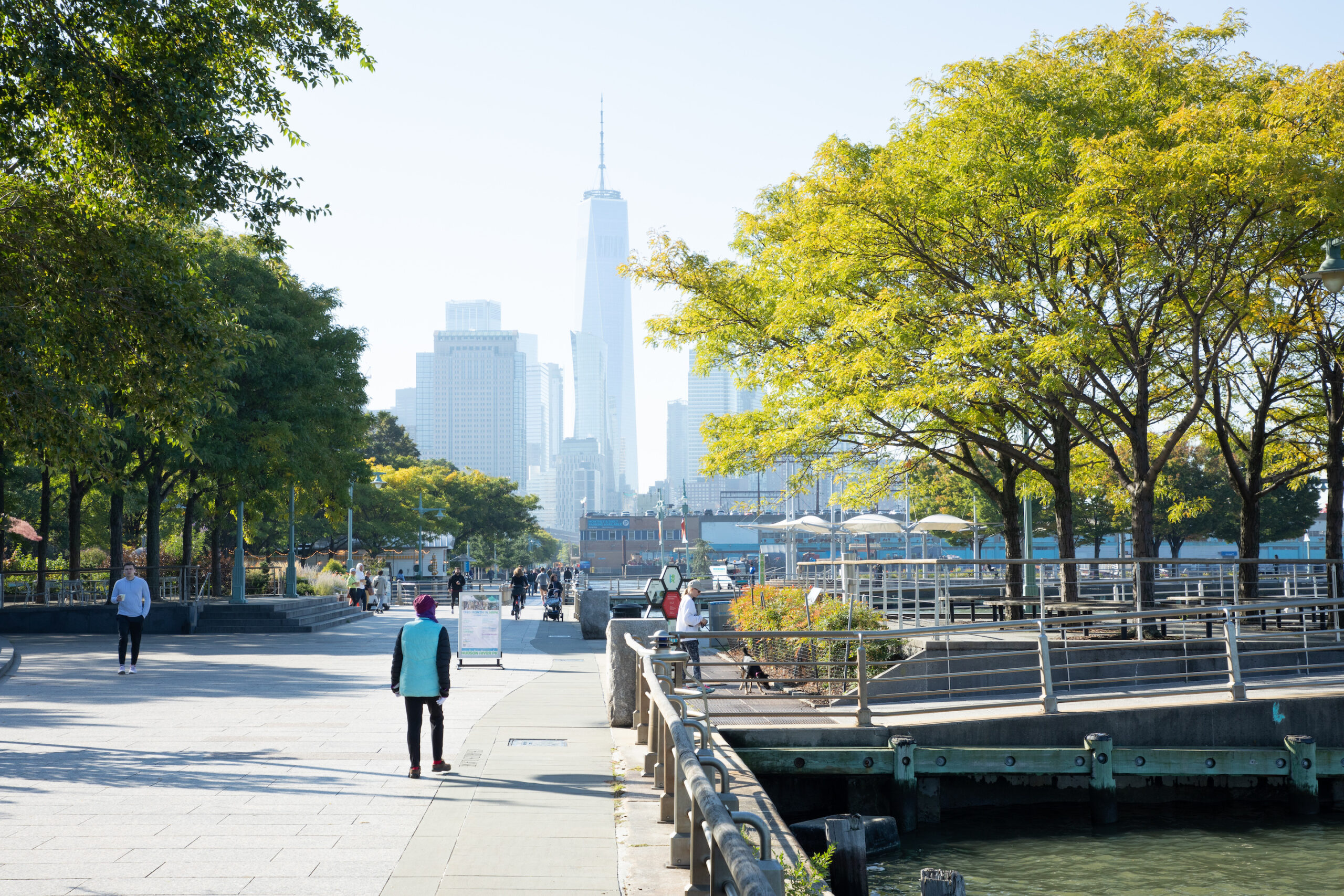 man walking down Hudson River Park riverfront esplanade alongside fall trees