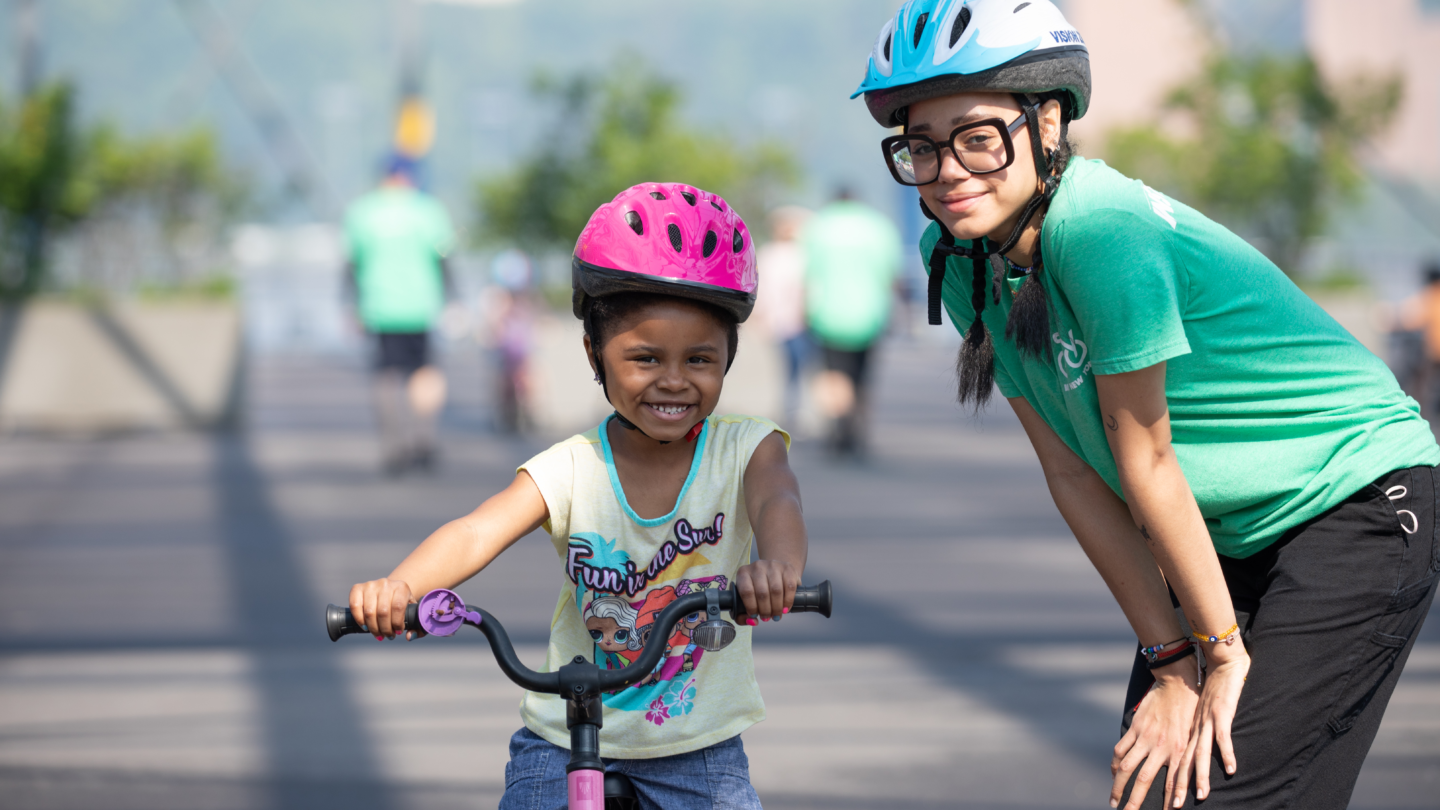 Bike Skills 101 at Pier 76, a girl on a bike and her instructor smile in helmets