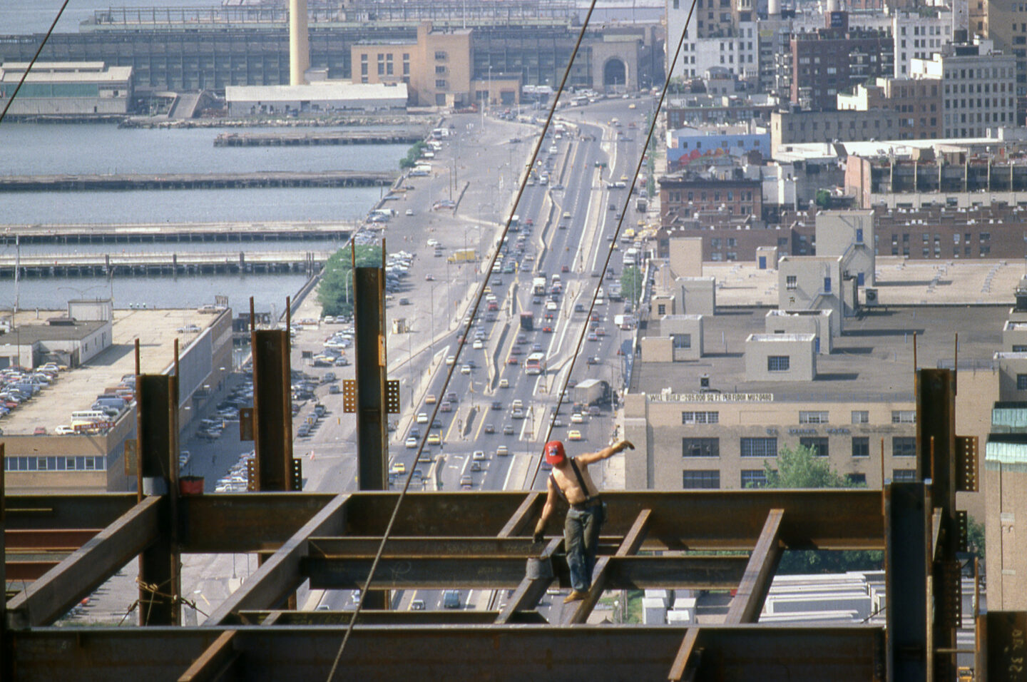 A construction worker walking along a beam high above the West Side Highway.