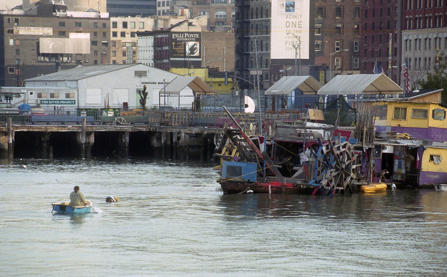 A person rowing toward a houseboad near Pier 25.
