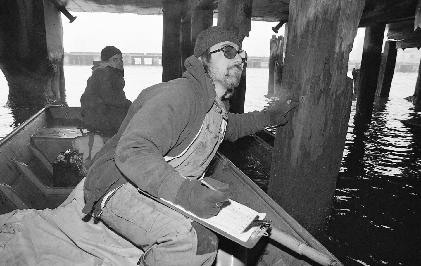 Two people in a rowboat inspecting the pilings underneath Pier 25.