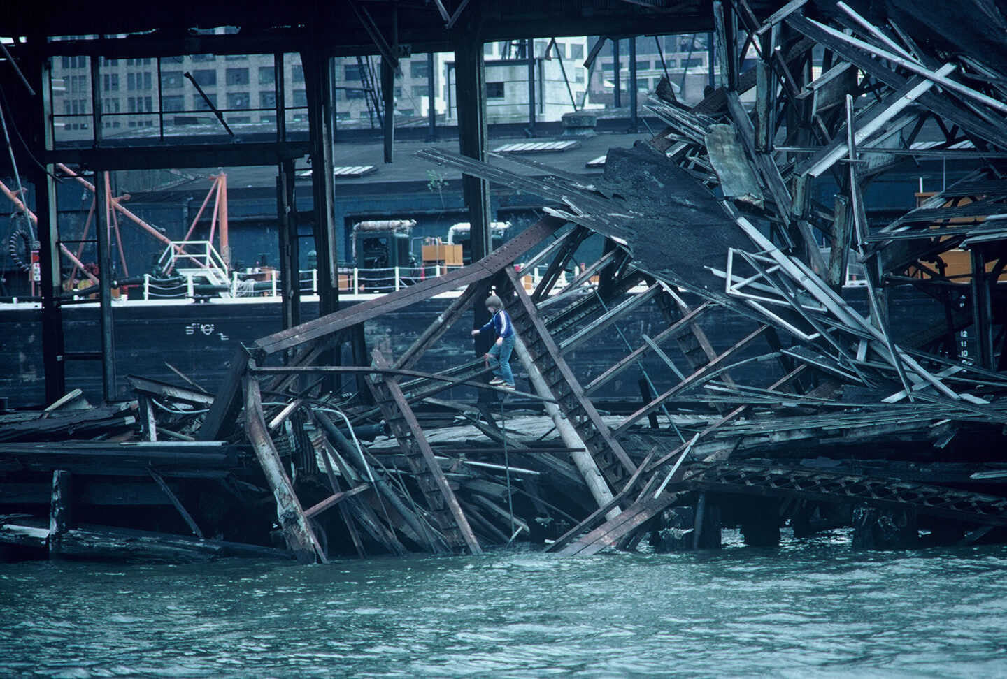 A boy climbing on the iron structure of a pier building that is collapsing into the Hudson River.