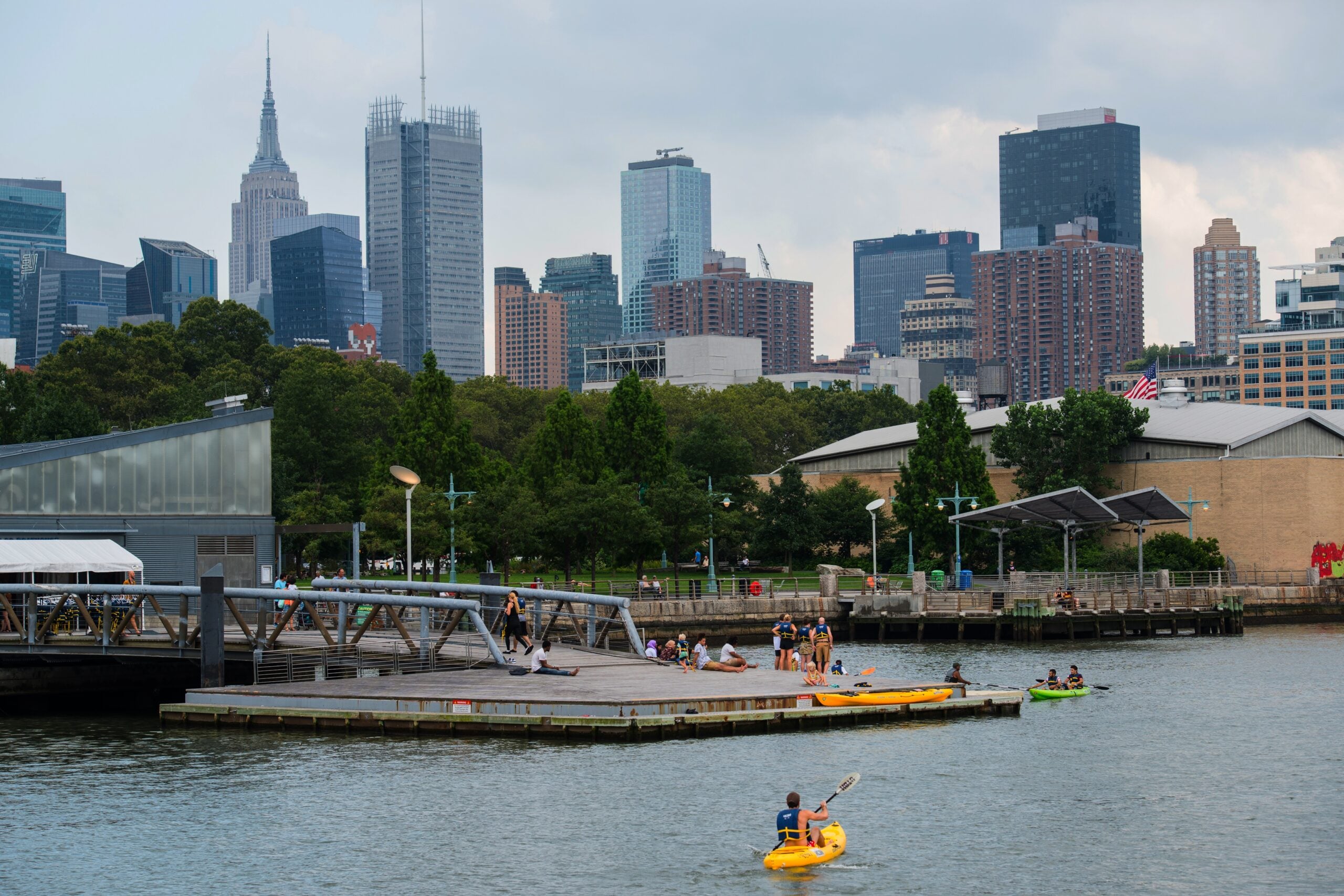 The boathouse dock with kayakers at Pier 96. Midtown skyscrapers are visible in the background.