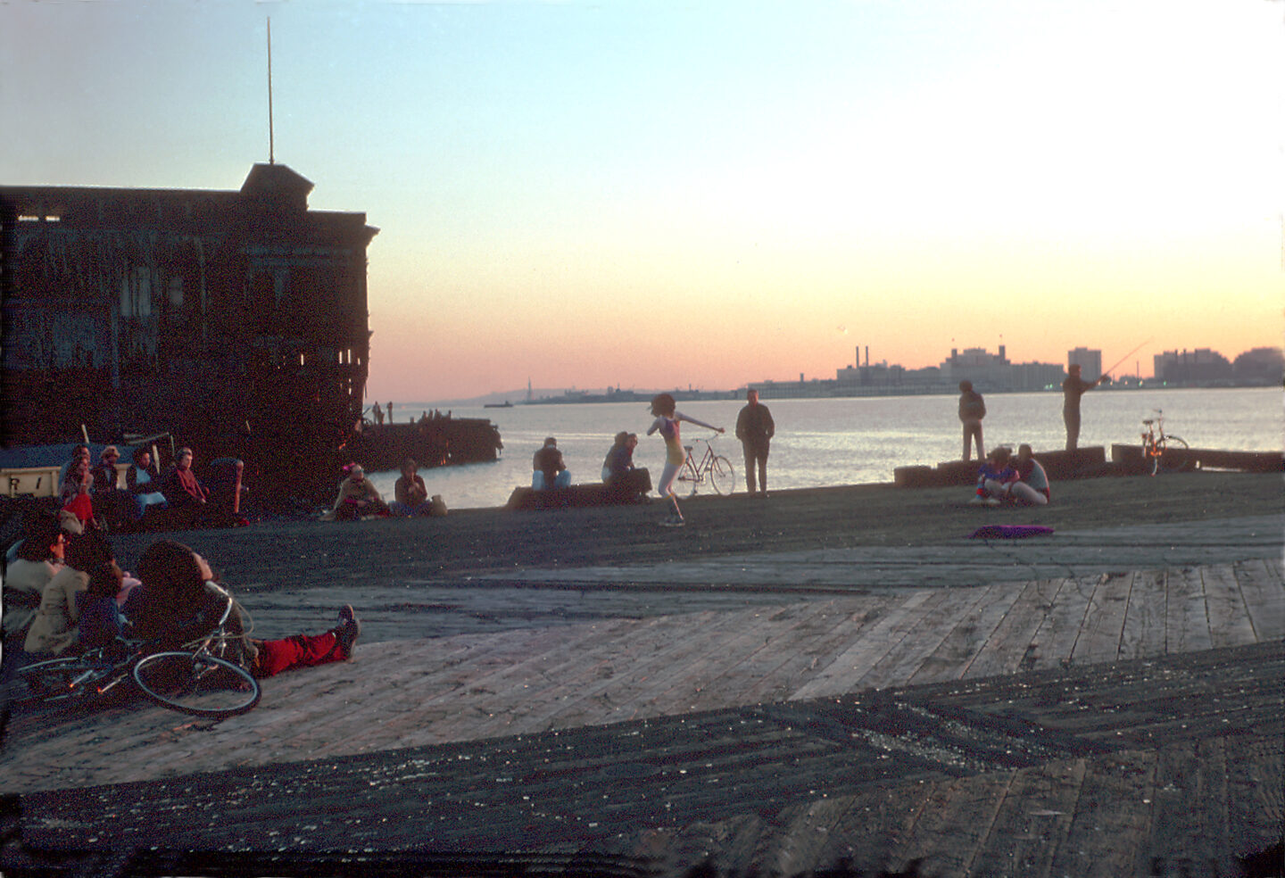 A dancer performs on a Hudson River pier at sunset as a small crowd watches.
