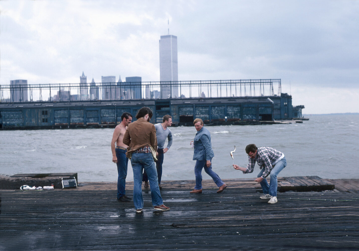 A fisherman pulls an eel onto a Hudson River pier while a group of fellow fishermen watch.