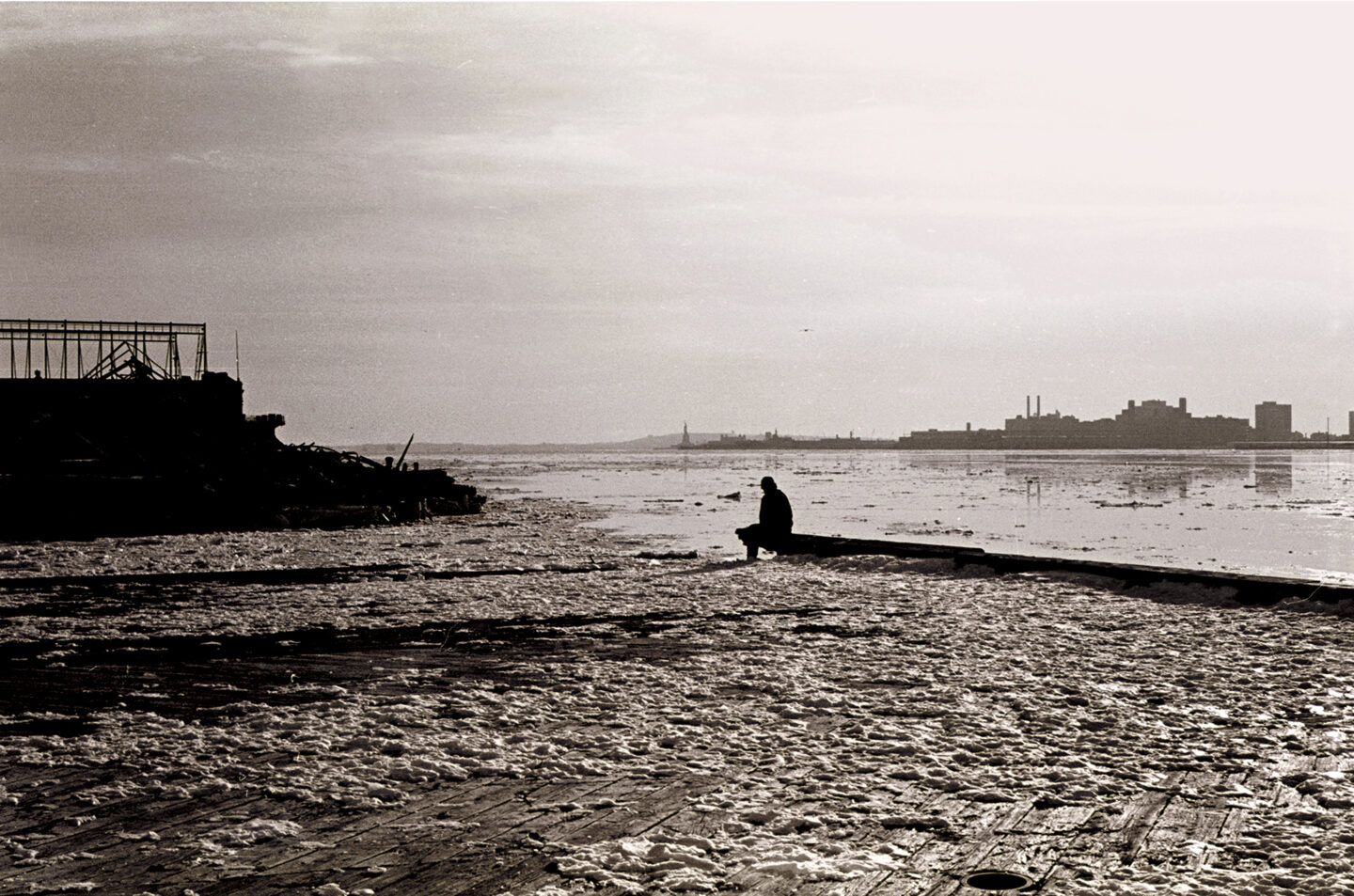 A person sits on the edge of a snowy pier.
