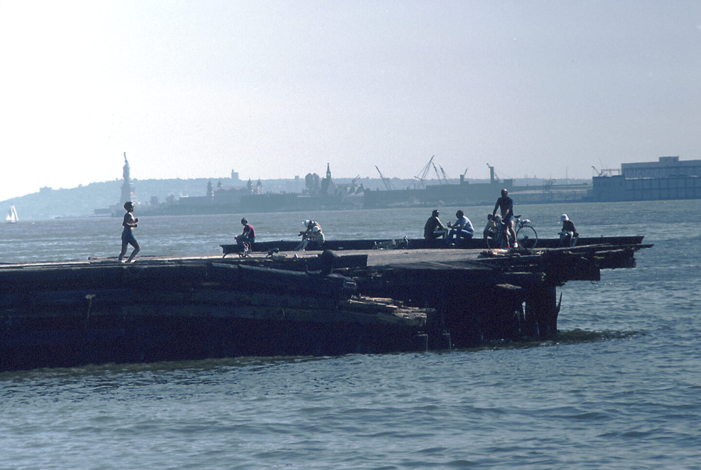 People hanging out on a Hudson River pier. The Statue of Liberty is visible in the distance.