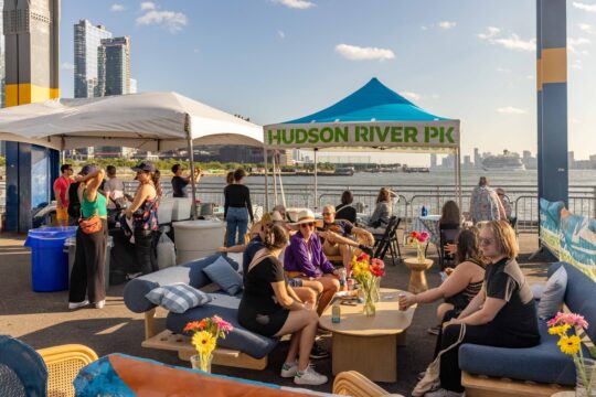 Groups gathered around tables in the Hudson River Park Friends VIP area at the Blues BBQ Festival at Pier 76