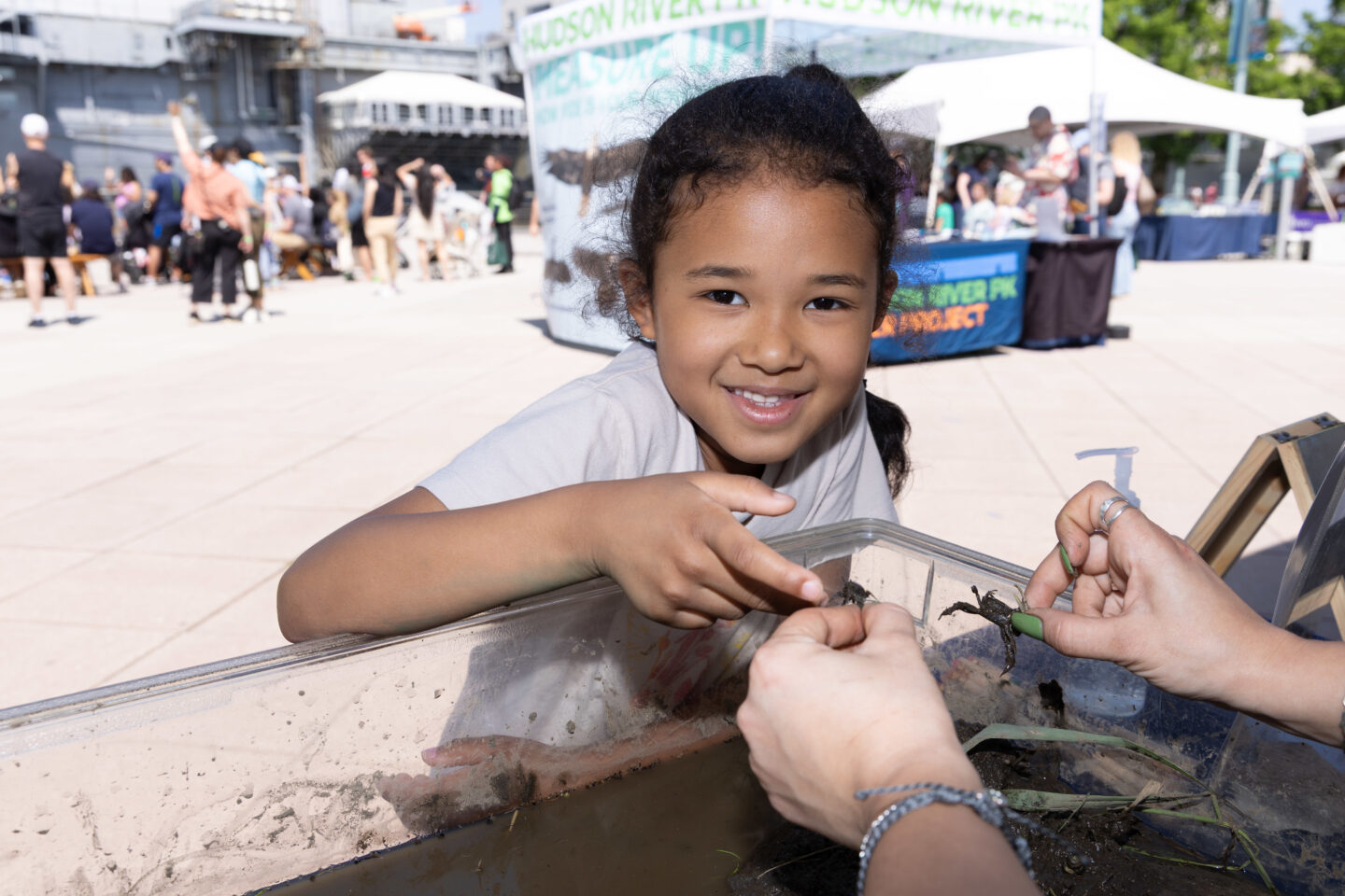 A student smiles and points to a small crab held in a SUBMERGE Marine Science Festival presenter's hand