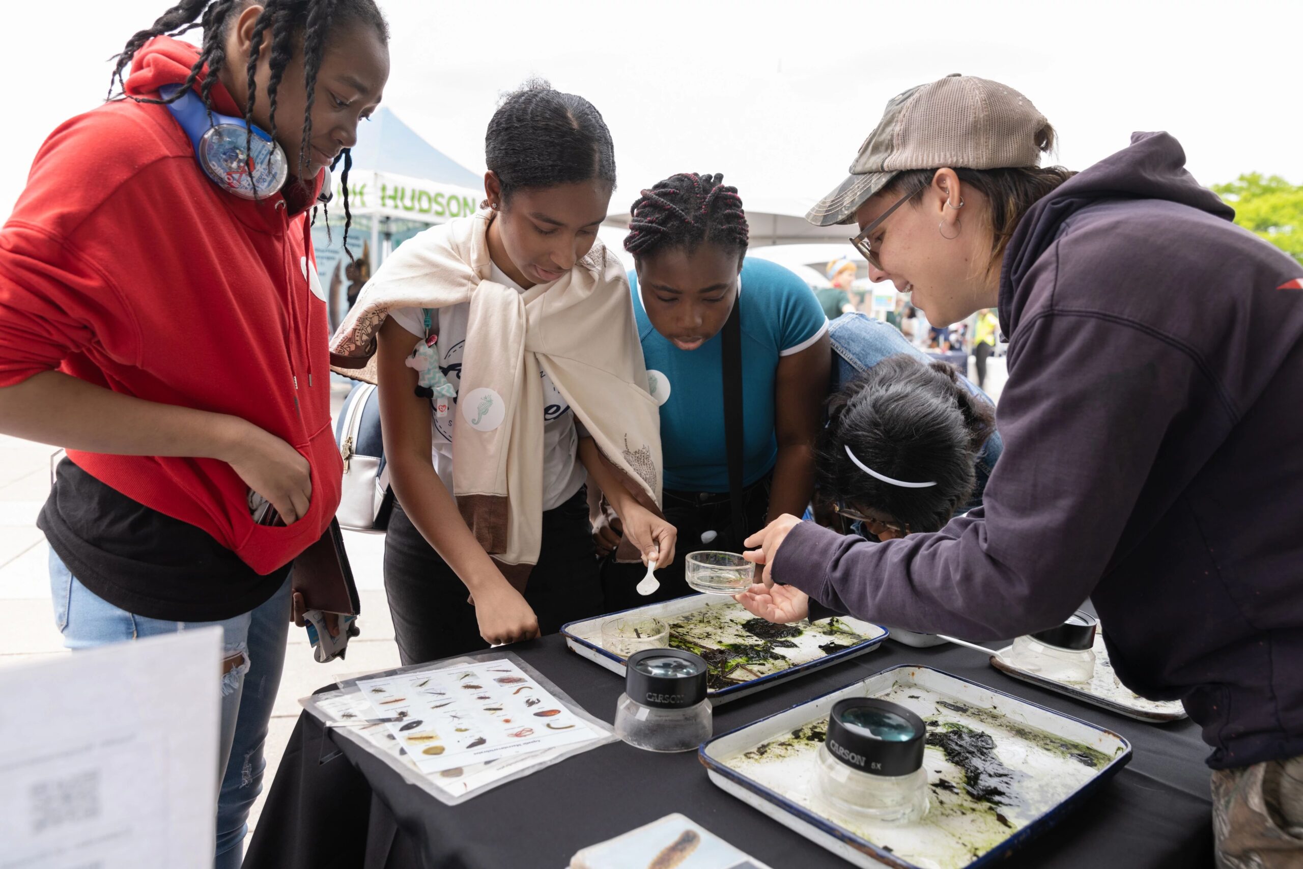 A group of students using loupe magnifying glasses to examine seaweed on a tray