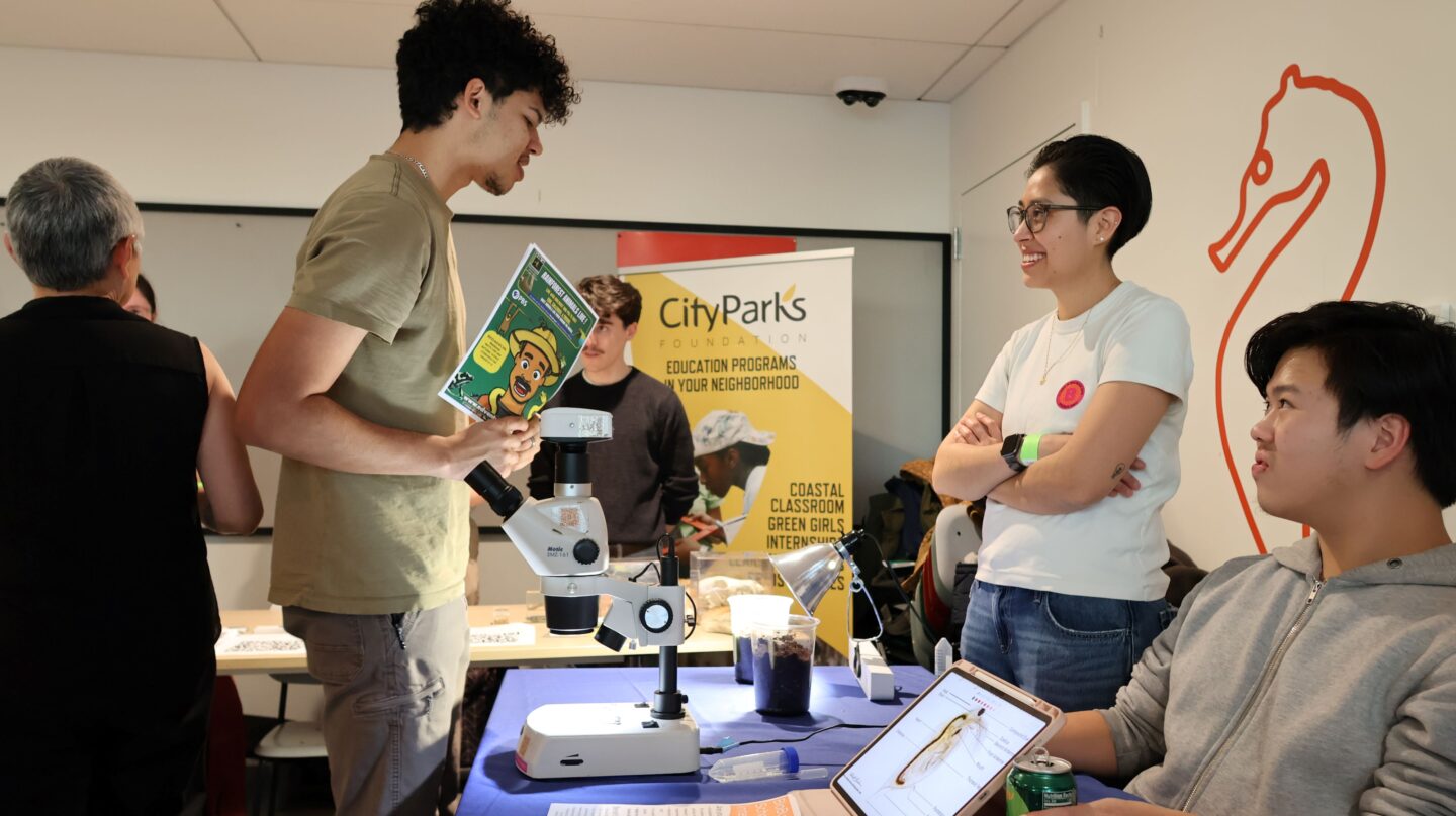 Two presenters speak at a table with an attendee at the NYC Outdoors Environmental Education Expo