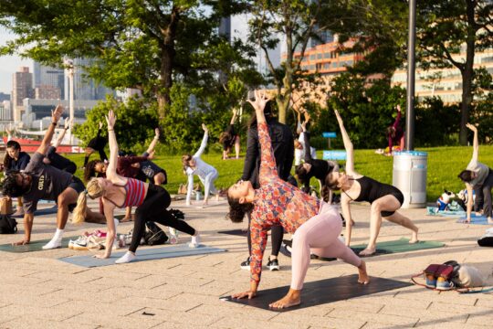 Healthy on the Hudson Yoga class participants hold a "Reverse Warrior" pose on Pier 64