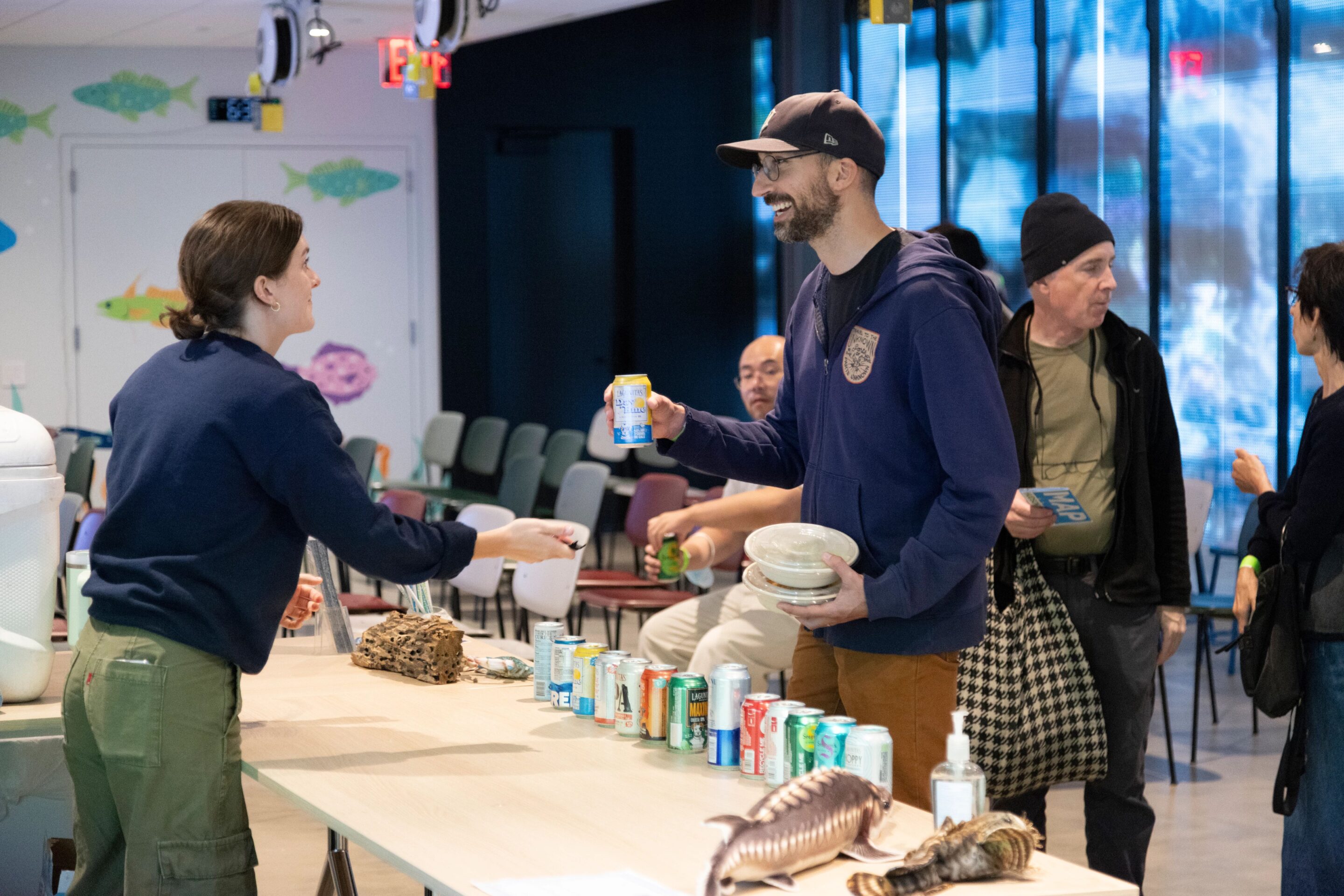 An HRPK River Project staffer hands a canned beverage to an attendee of an event at the Pier 57 Discovery Tank