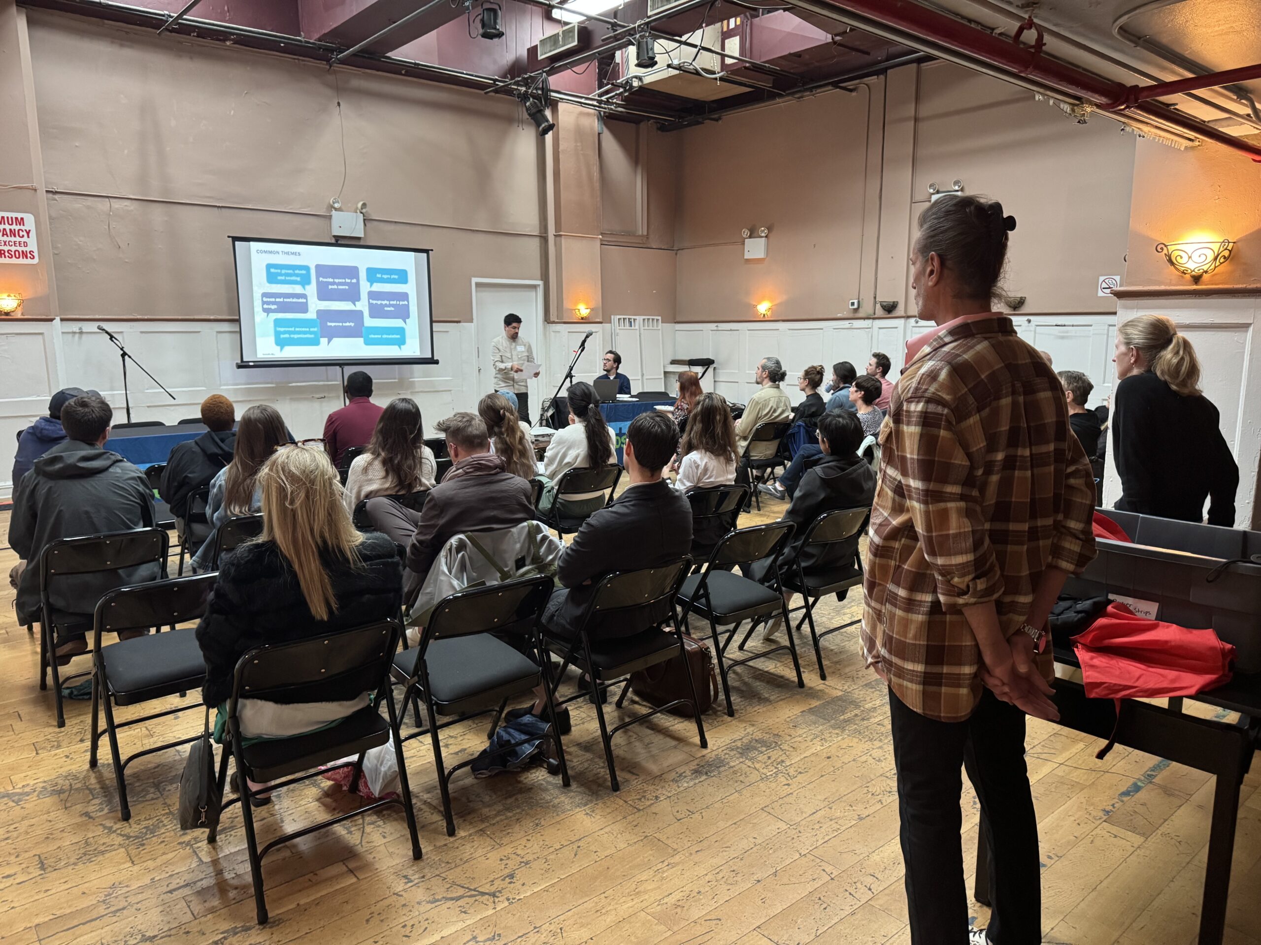 A seated and standing audience watches a slide deck presentation during a W 29–W 44 Esplanade & Landscape Engagement Meeting