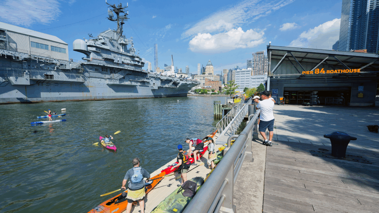 People kayaking at Pier 84, with the Intrepid Museum at Pier 86 visible in the background