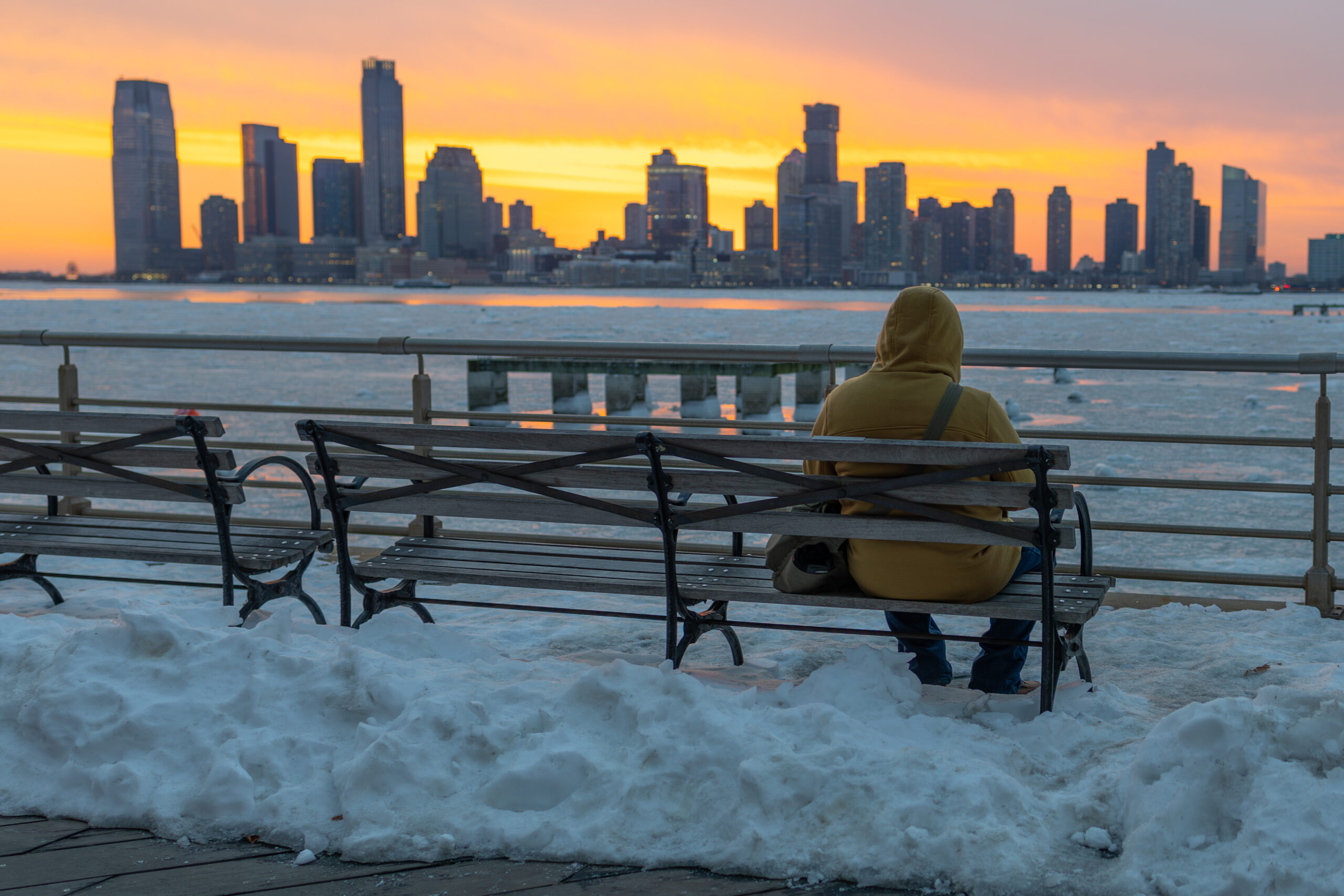 sunset over snowy waterfront, person on bench, in Tribeca in Hudson River Park
