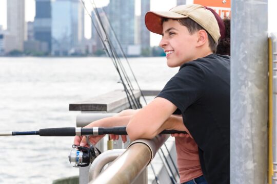 A person holds a fishing rod over a railing at Pier 26 during a Big City Fishing event