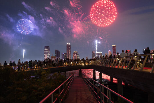 Crowds gather at the edge of Pier 26 to watch red and blue fireworks over the Hudson River