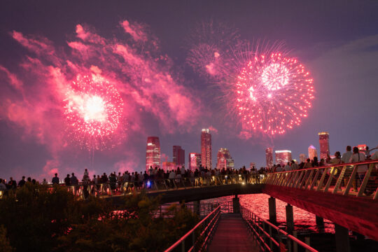Crowds gather at the edge of Pier 26 to watch red fireworks over the Hudson River