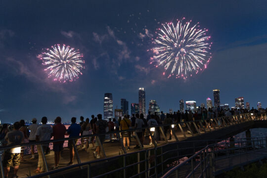 Crowds gather at the edge of Pier 26 to watch white and red fireworks over the Hudson River