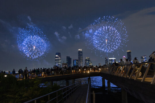 Crowds gather at the edge of Pier 26 to watch blue fireworks over the Hudson River