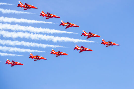 Red planes soar overhead in blue sky leaving trail of white