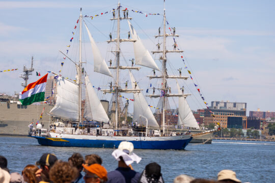 People gather at edge of a pier to watch tall ship sailing Hudson River