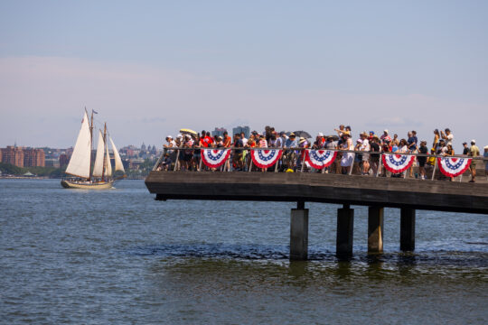 Crowds gather at edge of Pier 26 as a sailboat sails by in Hudson River